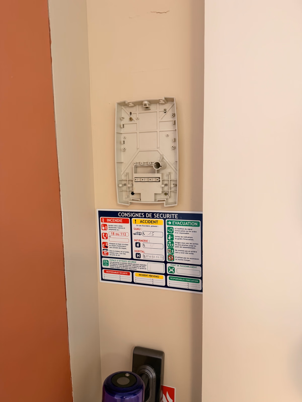 Boîtier d'alarme incendie type 4 démonté sur un mur, bouton poussoir défectueux visible, à côté d'une affiche de consignes de sécurité, salle de fitness à Royan