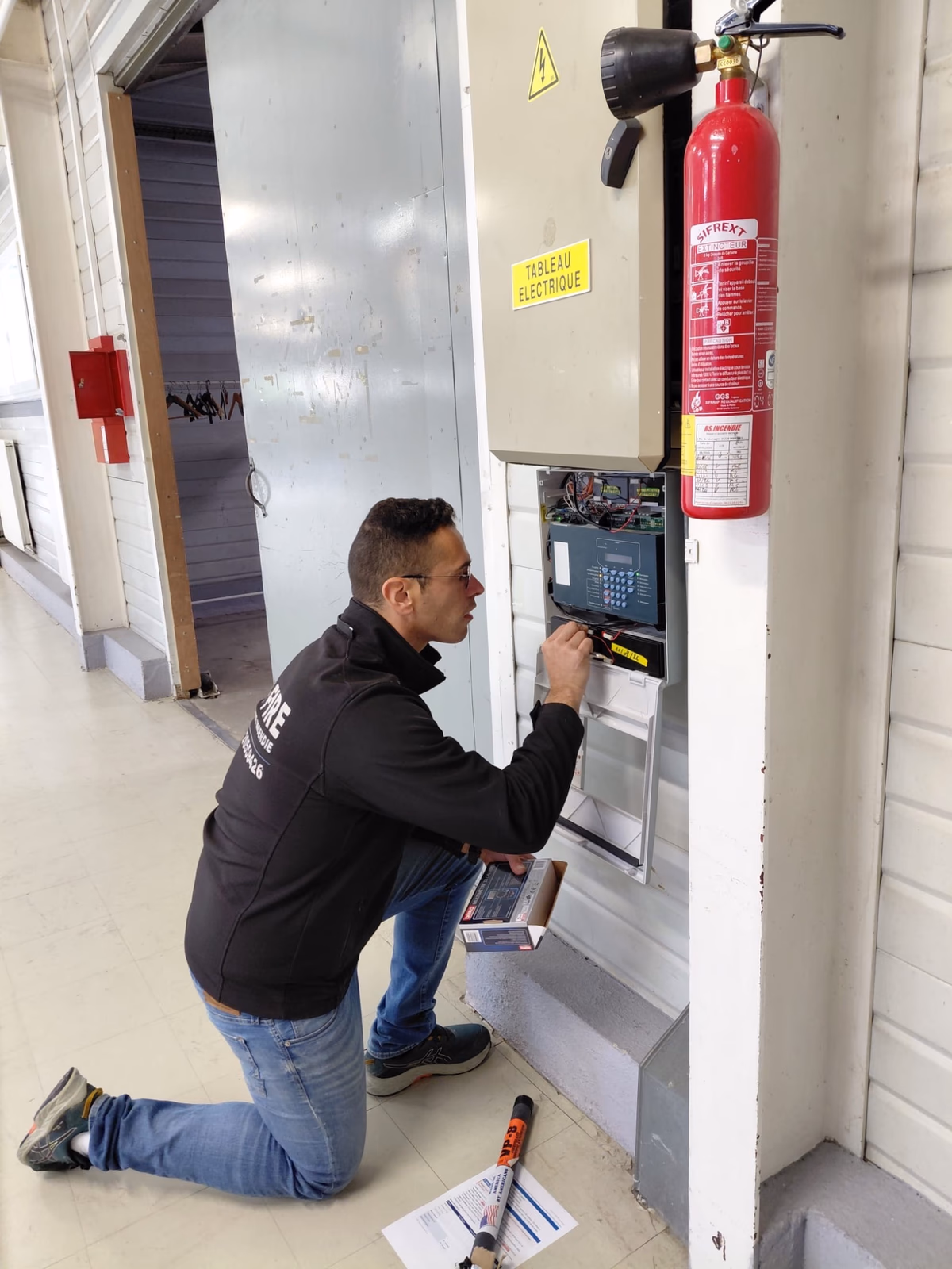 Technicien FJ Fire installant la centrale d'alarme incendie près du tableau électrique et d'un extincteur CO2, salle de réception à Saint-Seurin-sur-l'Isle
